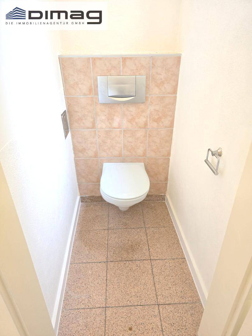 Separate Toilette mit wandhängendem WC und beigefarbenen Fliesen.