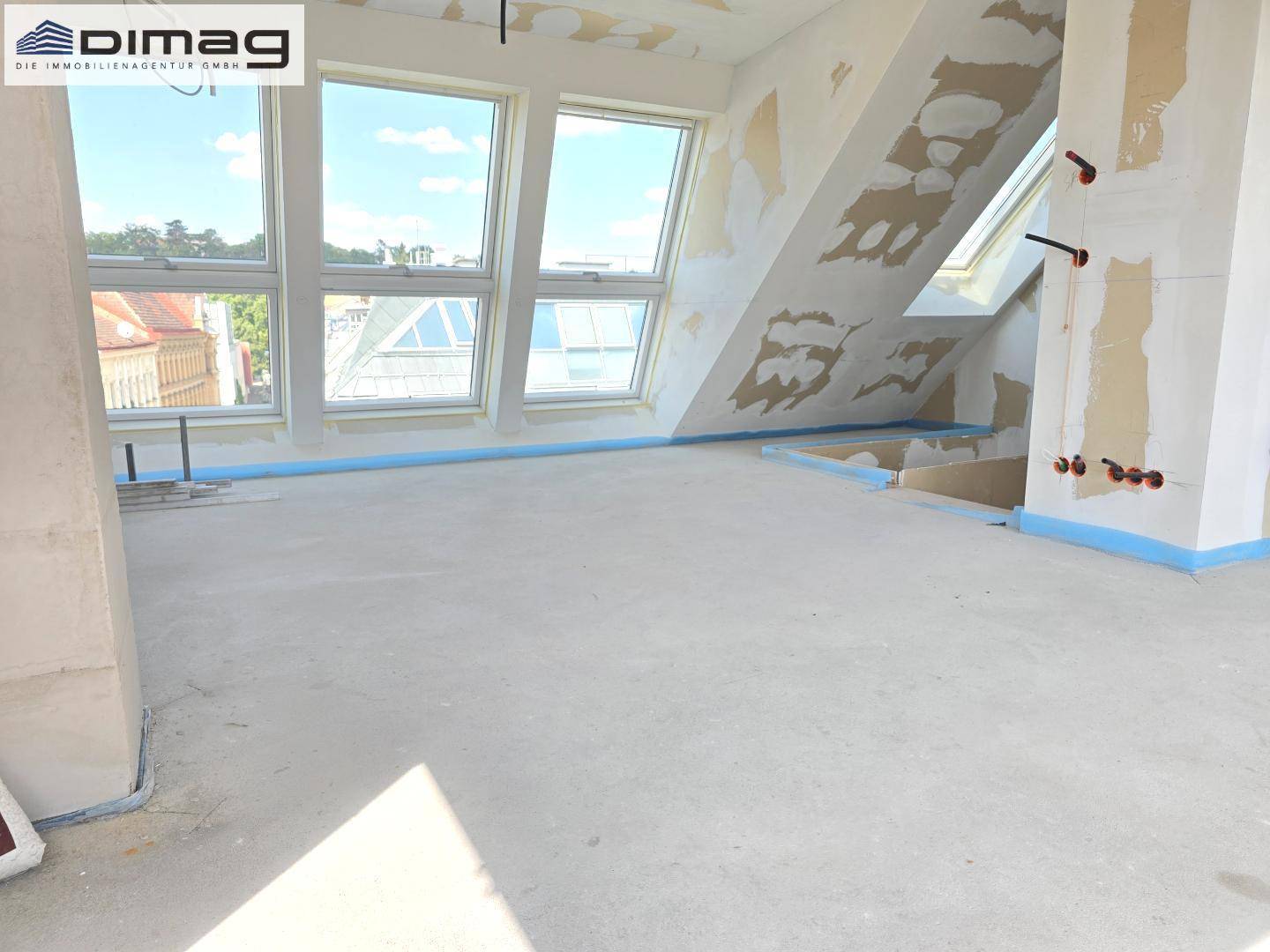 Heller Rohbau-Raum mit mehreren Dachfenstern und Betonboden, ideal für den weiteren Ausbau.