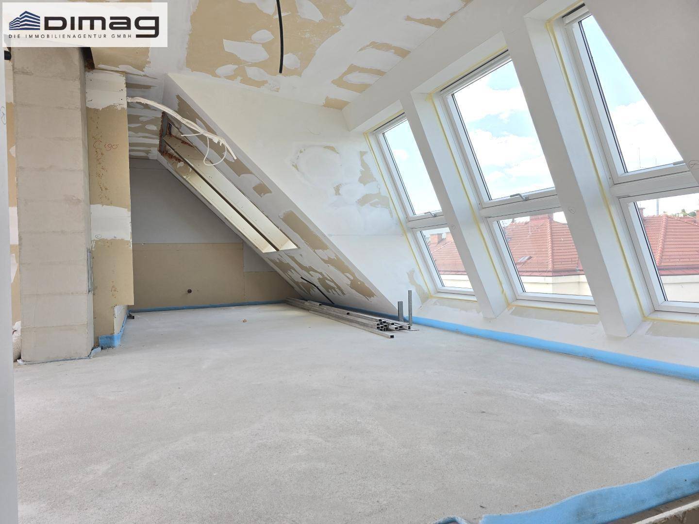 Geräumiger Rohbau-Raum mit schrägen Wänden, Dachfenstern und Betonboden, wartet auf Fertigstellung.