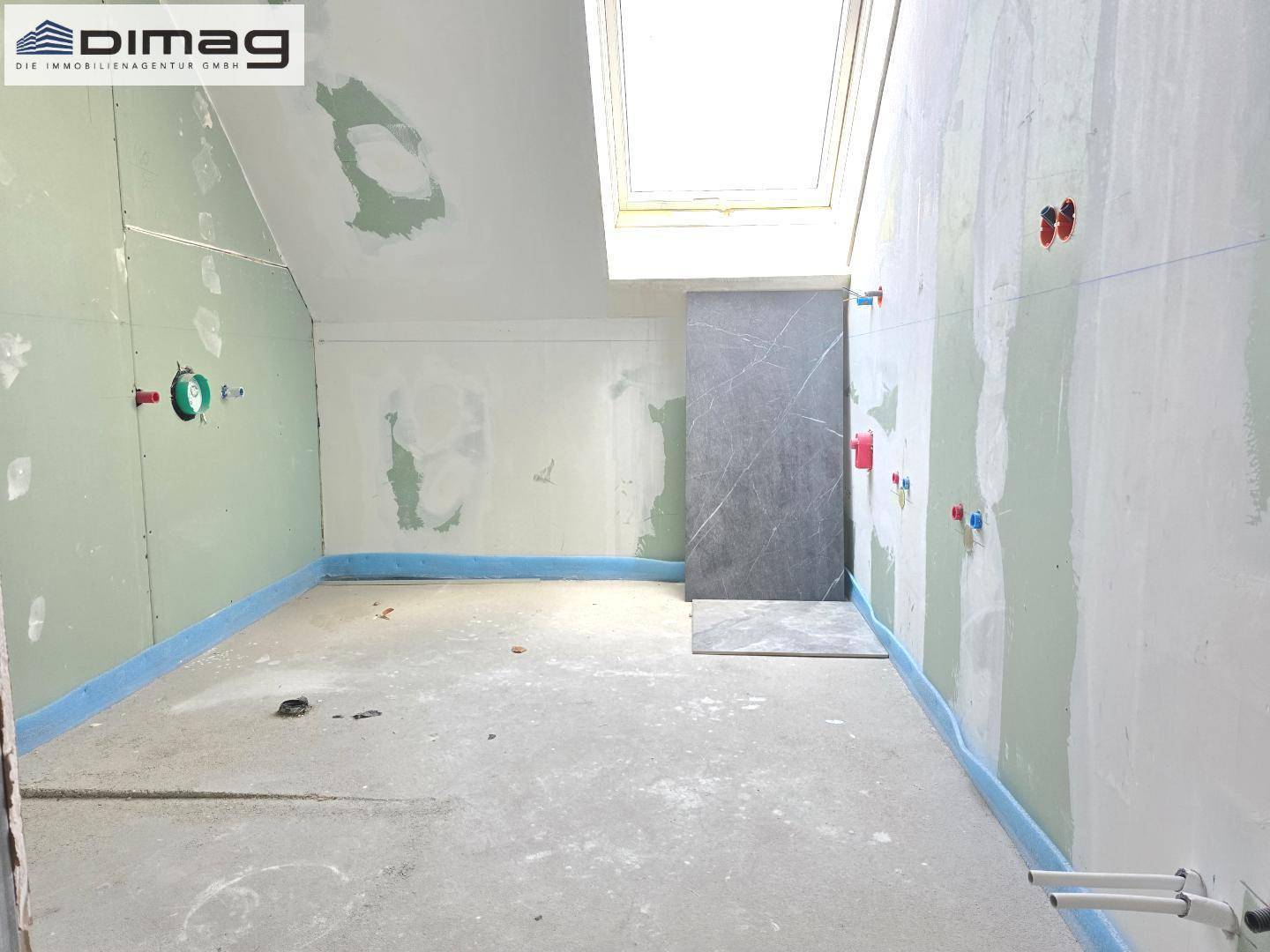 Rohbau-Badezimmer mit Dachfenster und vorbereiteten Anschlüssen, wartet auf die Endmontage.