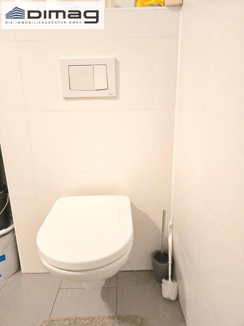 Modernes WC mit wandhängender Toilette und hellen Fliesen an Wänden und Boden.