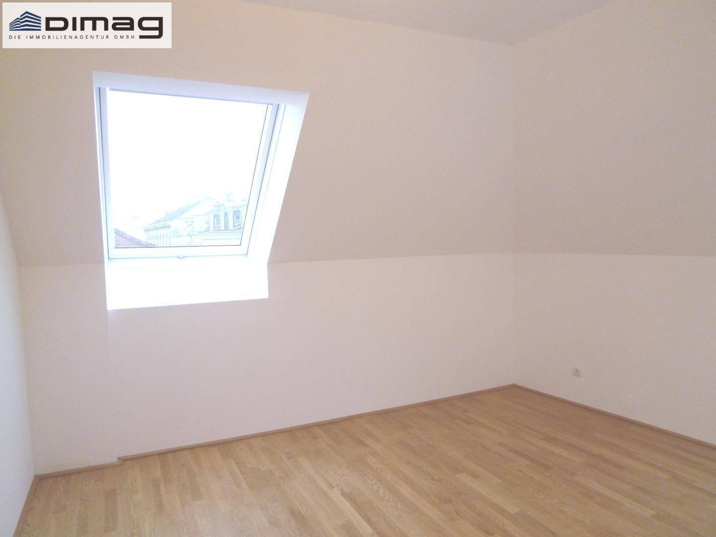 Gemütliches Dachgeschosszimmer mit einem großen Dachfenster und hellem Parkettboden.