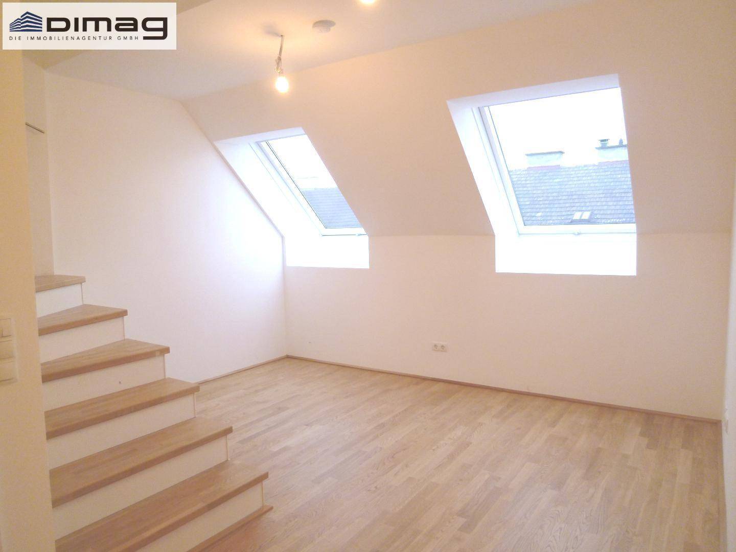 Heller Dachgeschossraum mit Holztreppe, zwei Dachfenstern und hellem Parkettboden.