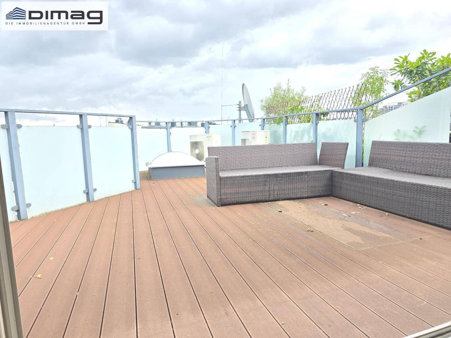 Weitläufige Holzterrasse mit modernen Outdoor-Sitzmöbeln und Glasgeländer unter bewölktem Himmel.