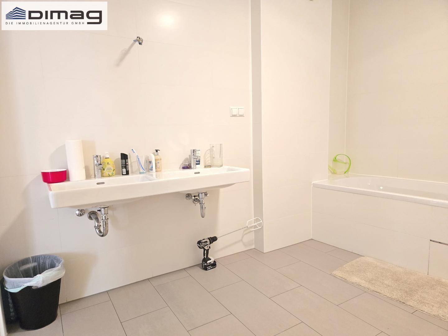 Modernes Badezimmer mit Doppelwaschbecken, Badewanne und hellen Fliesen an Wänden und Boden.