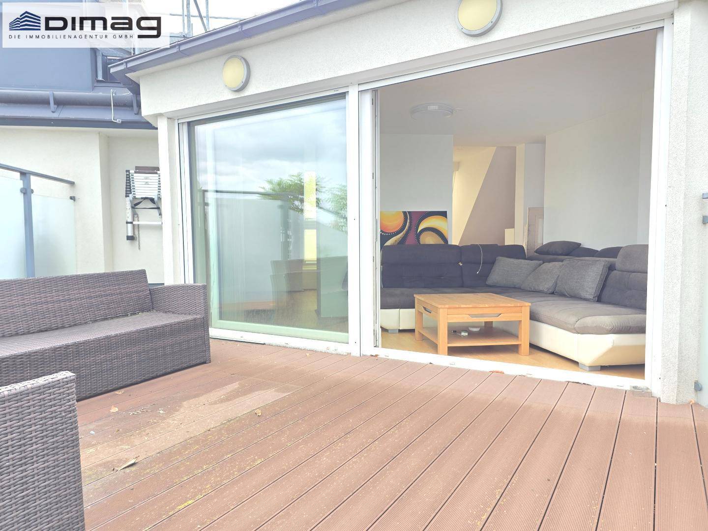 Große Holzterrasse mit Outdoor-Sitzmöbeln und Zugang zum Wohnbereich durch eine Glasschiebetür.