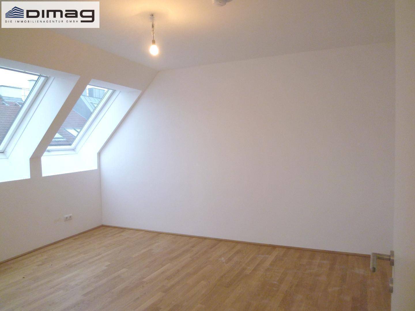 Helles Dachgeschosszimmer mit zwei Dachfenstern und sauberem, hellem Parkettboden.