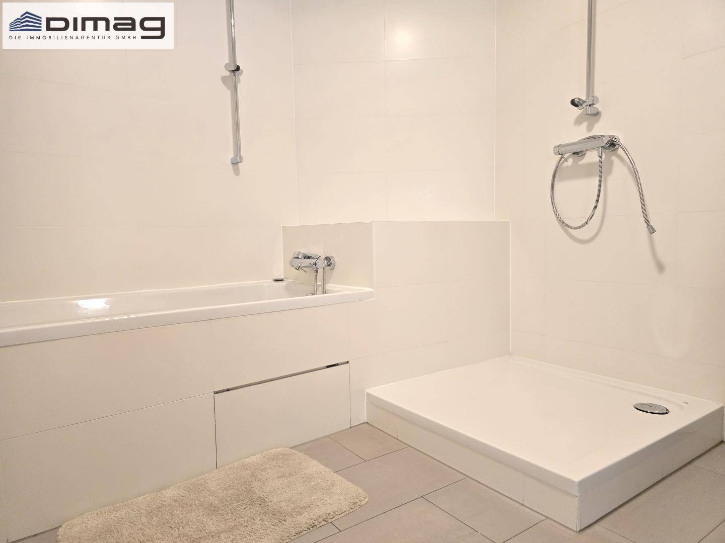 Modernes Badezimmer mit Badewanne, ebenerdiger Dusche und hellen Fliesen an Wänden und Boden.