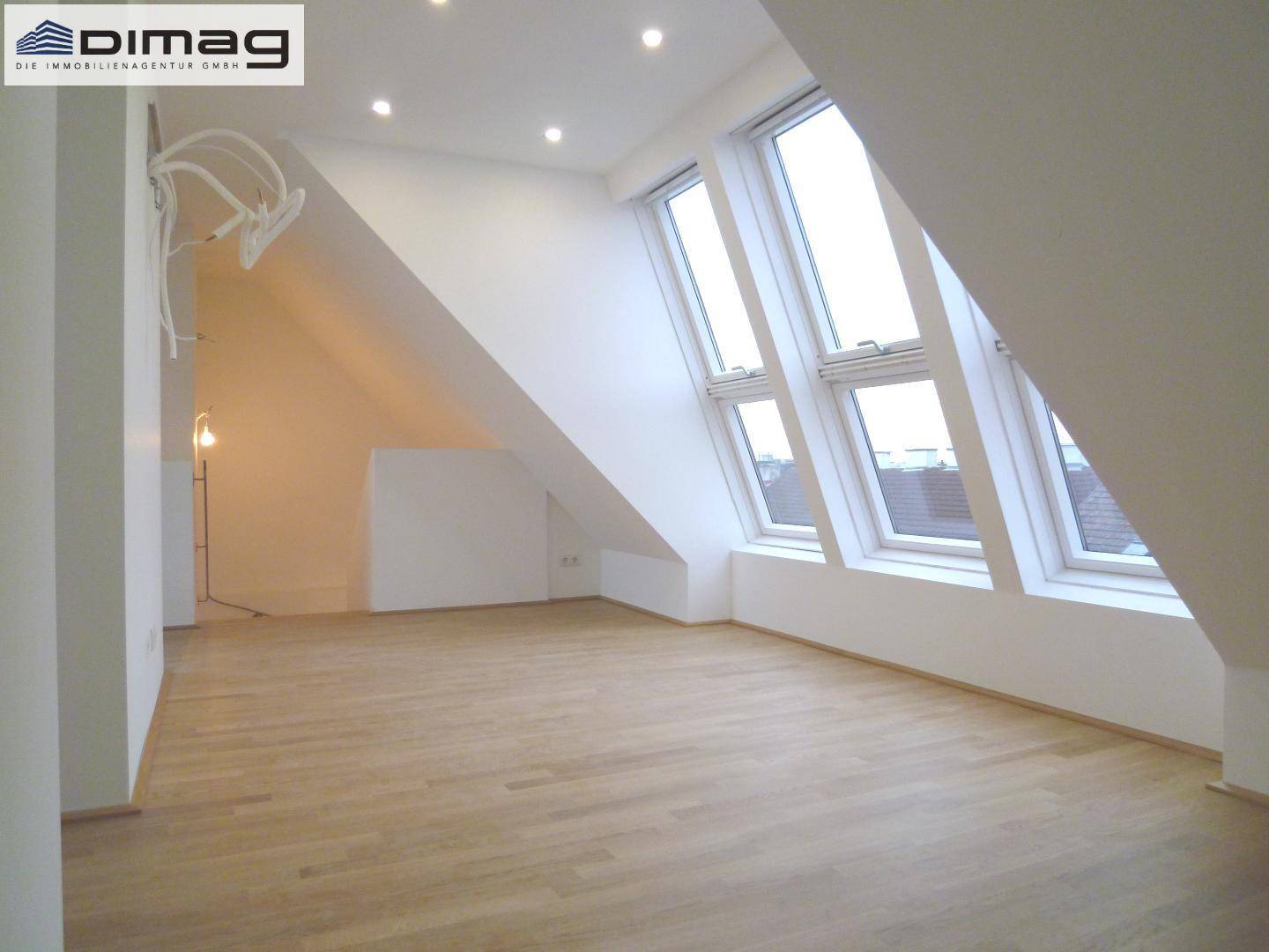 Helles Dachgeschosszimmer mit schrägen Wänden, Einbaustrahlern und hellem Holzparkettboden.