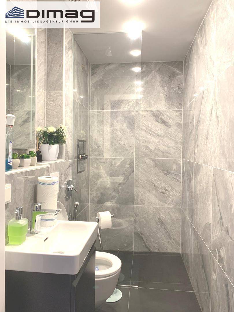 Modernes Gäste-WC mit grauen Fliesen, wandhängendem WC und kleinem Waschbecken.