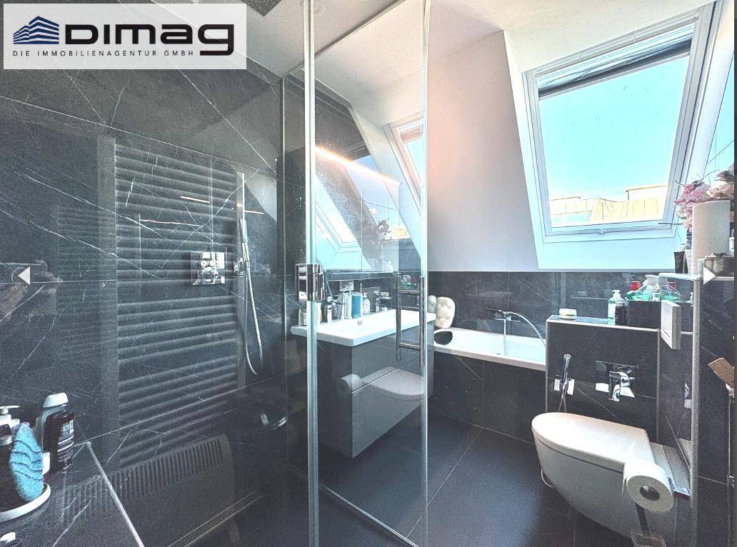 Modernes Badezimmer mit dunklen Fliesen, Badewanne und Dachfenster für Tageslicht.
