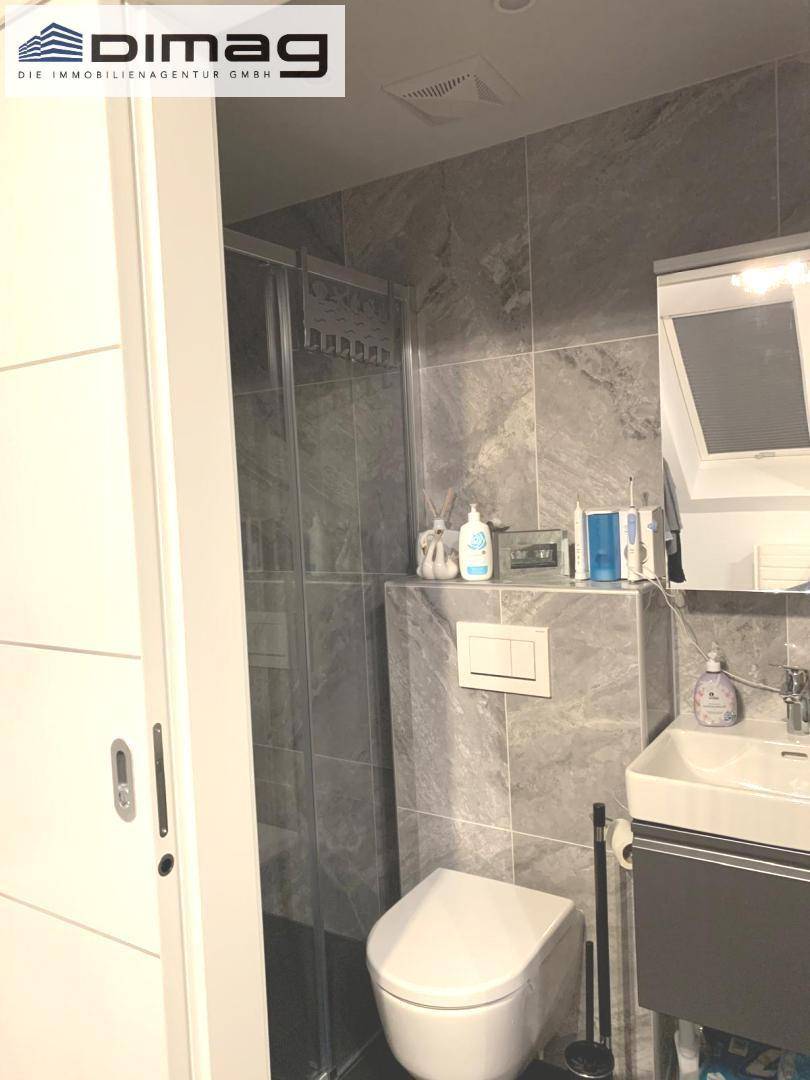Kleines Badezimmer mit Dusche, WC und Waschbecken, komplett gefliest in Grau.