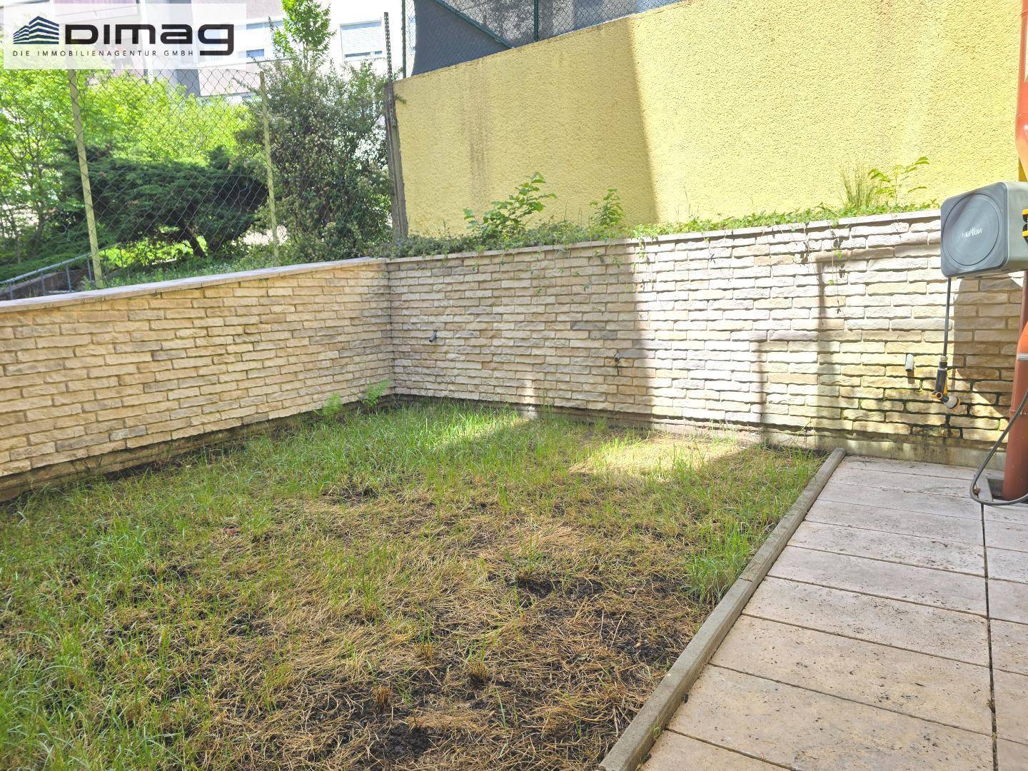 Kleiner privater Gartenbereich mit Rasenfläche und einer schützenden Steinmauer.