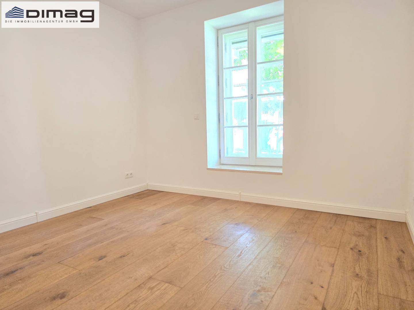 Geräumiges Zimmer mit Holzboden und großem Fenster für viel Tageslicht und eine angenehme Atmosphäre.