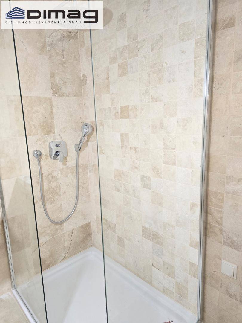 Duschbereich mit Glasabtrennung und beigefarbenen Fliesen im modernen Badezimmer.