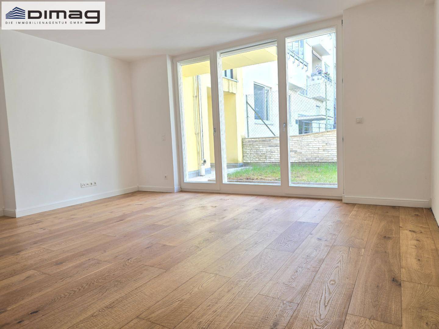 Geräumiges Zimmer mit Holzboden und großen Fenstern, die Zugang zu einem Außenbereich bieten.