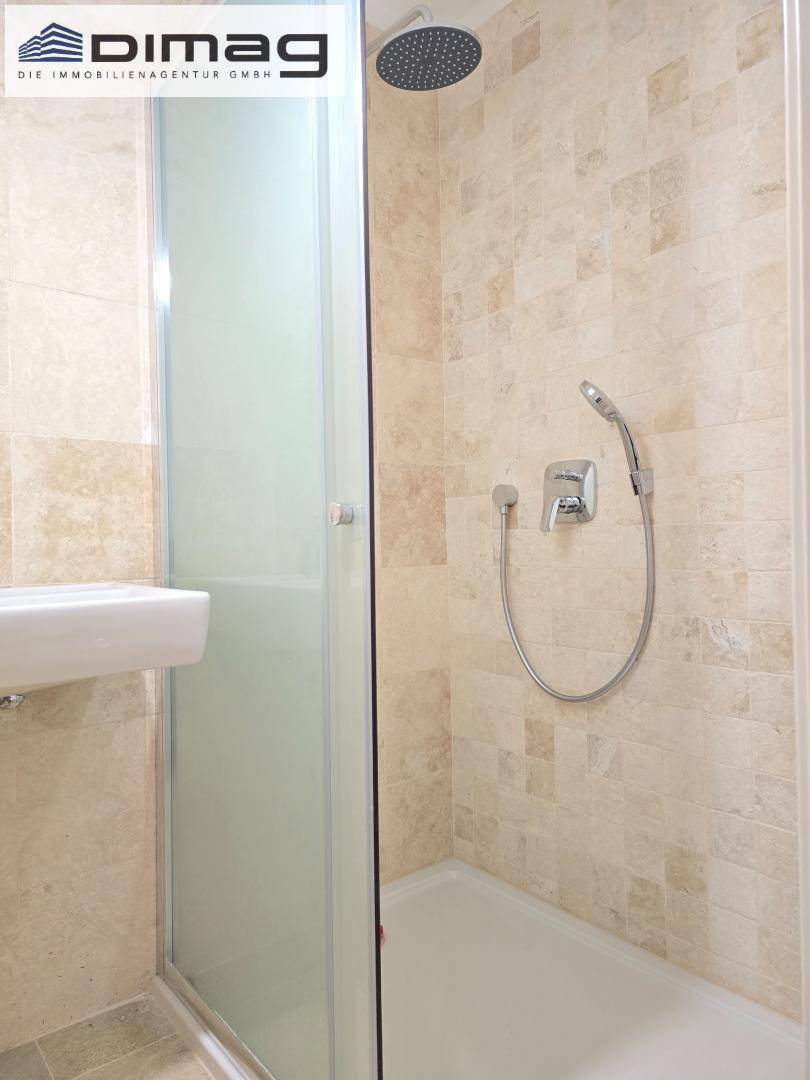 Modernes Badezimmer mit Duschkabine, Regendusche und beigefarbenen Fliesen an Wänden und Boden.