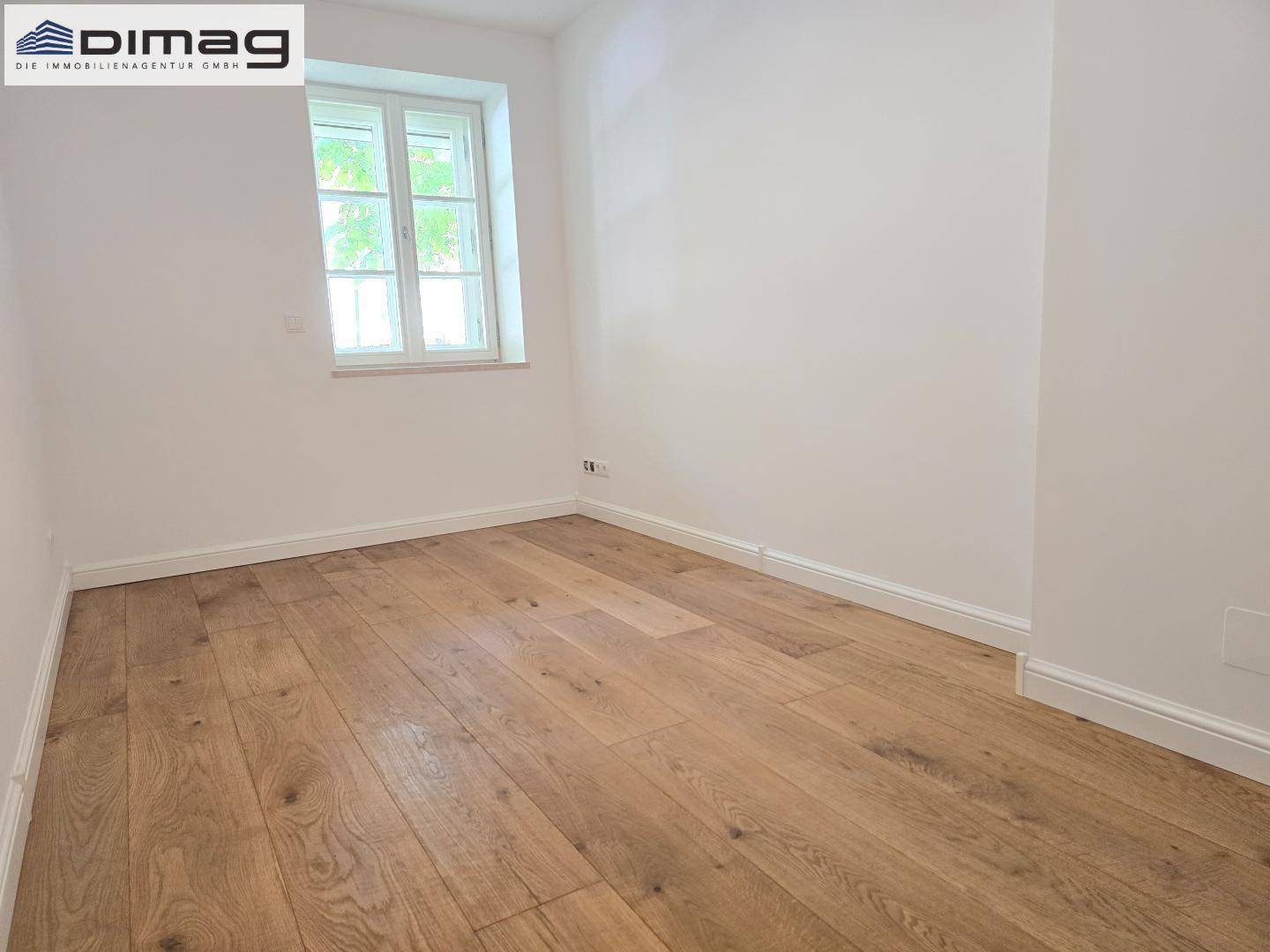 Helles Zimmer mit Holzboden und einem Fenster, geeignet als Schlaf- oder Kinderzimmer.