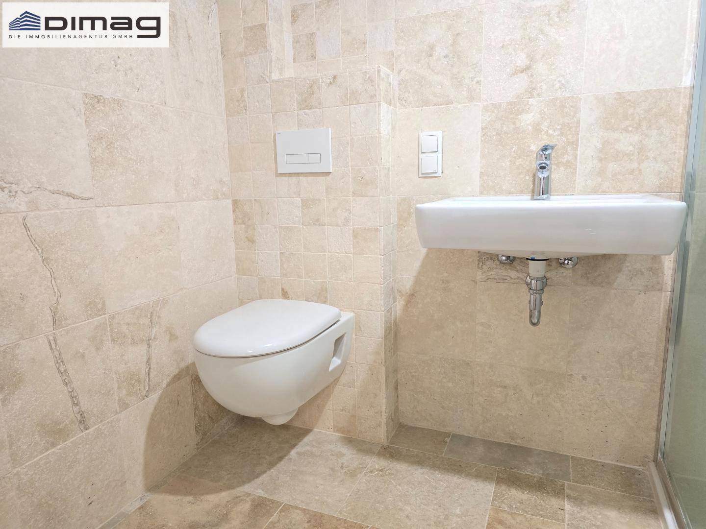 Badezimmer mit Wand-WC, modernem Waschbecken und beigefarbenen Fliesen im gesamten Raum.