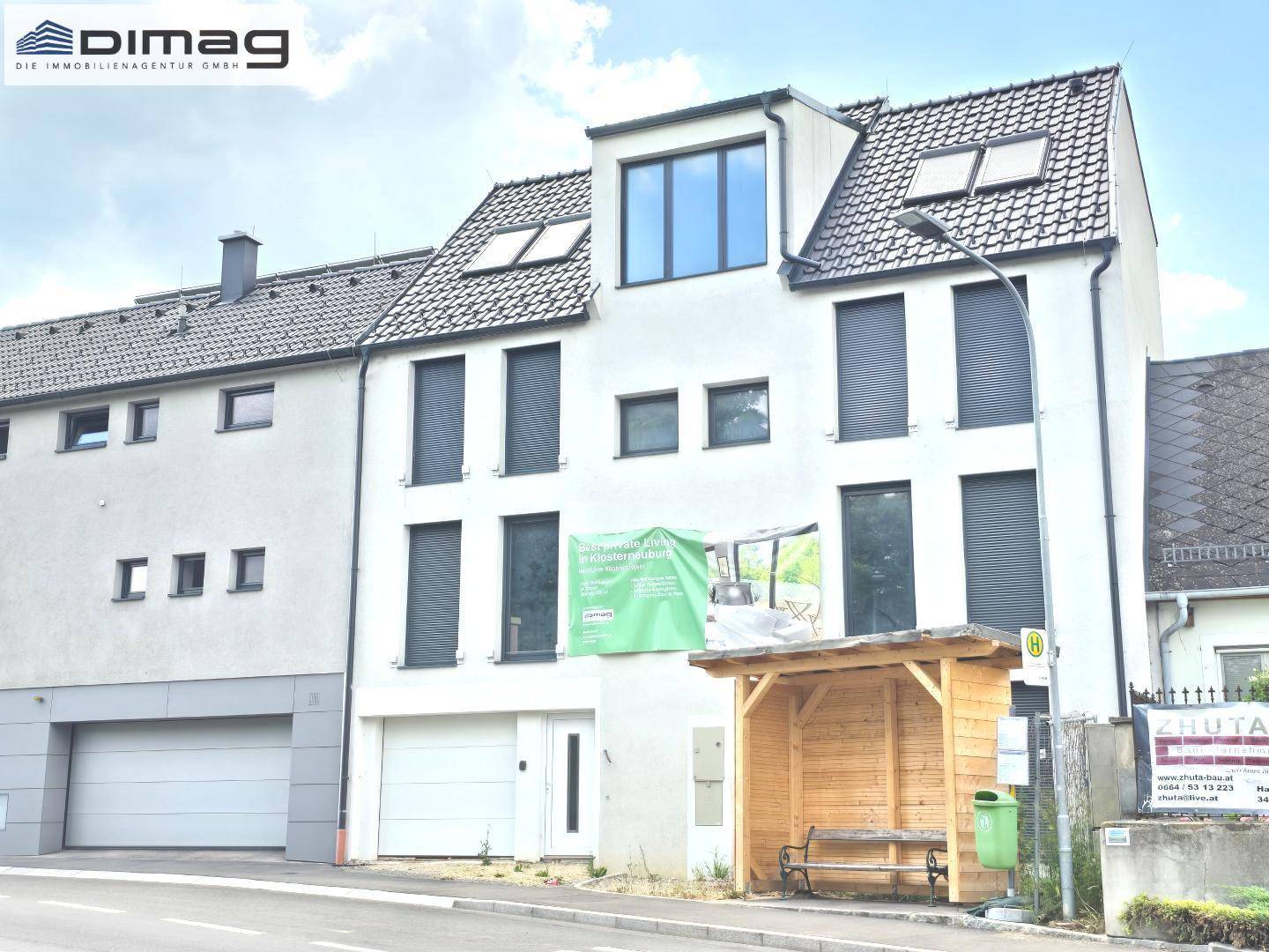 Ansicht eines modernen Wohnhauses mit weißer Fassade, dunklen Fensterläden und Dachgauben.
