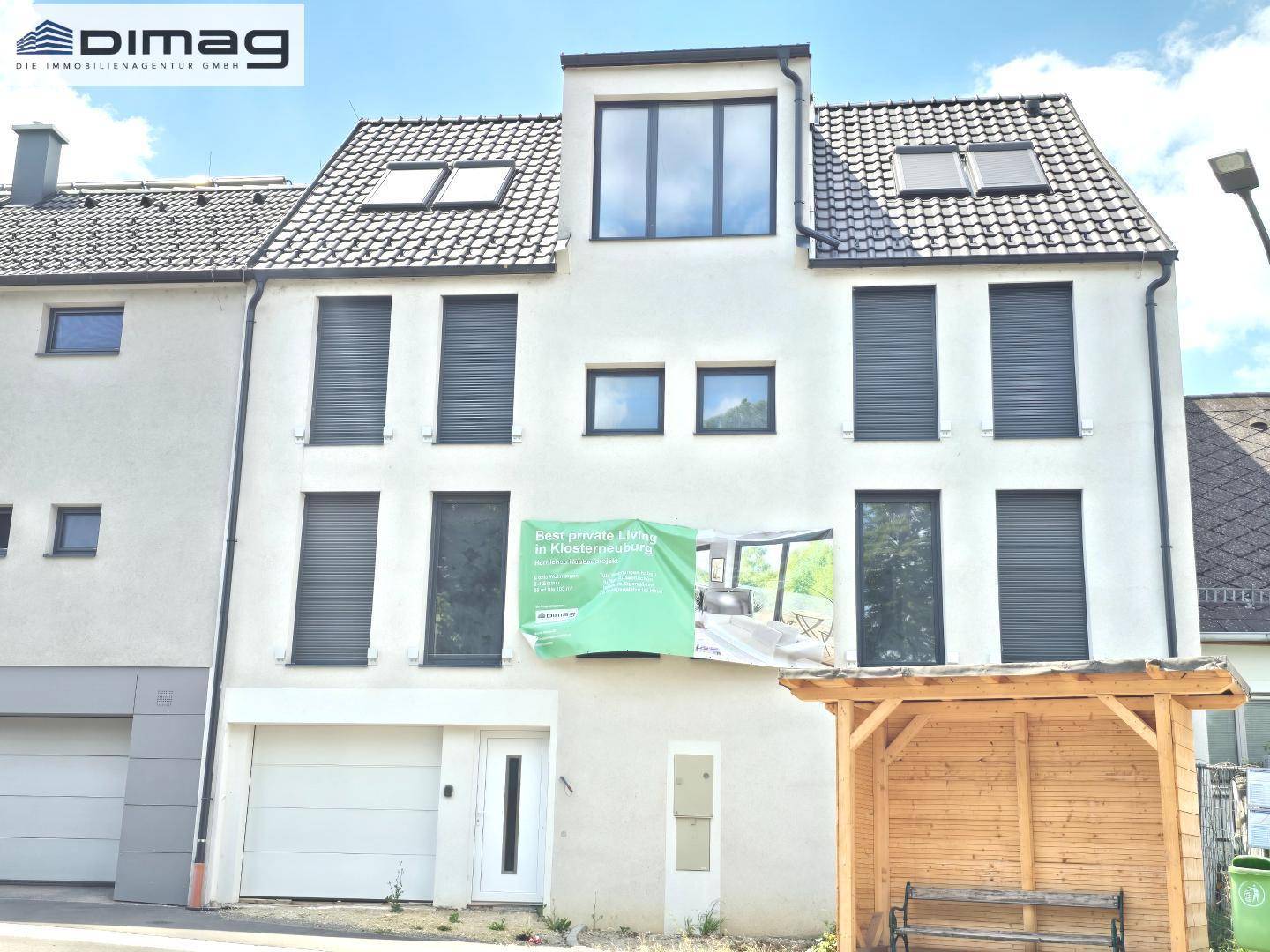 Vorderansicht eines modernen Gebäudes mit weißer Fassade, dunklen Fensterläden und Garagentor.