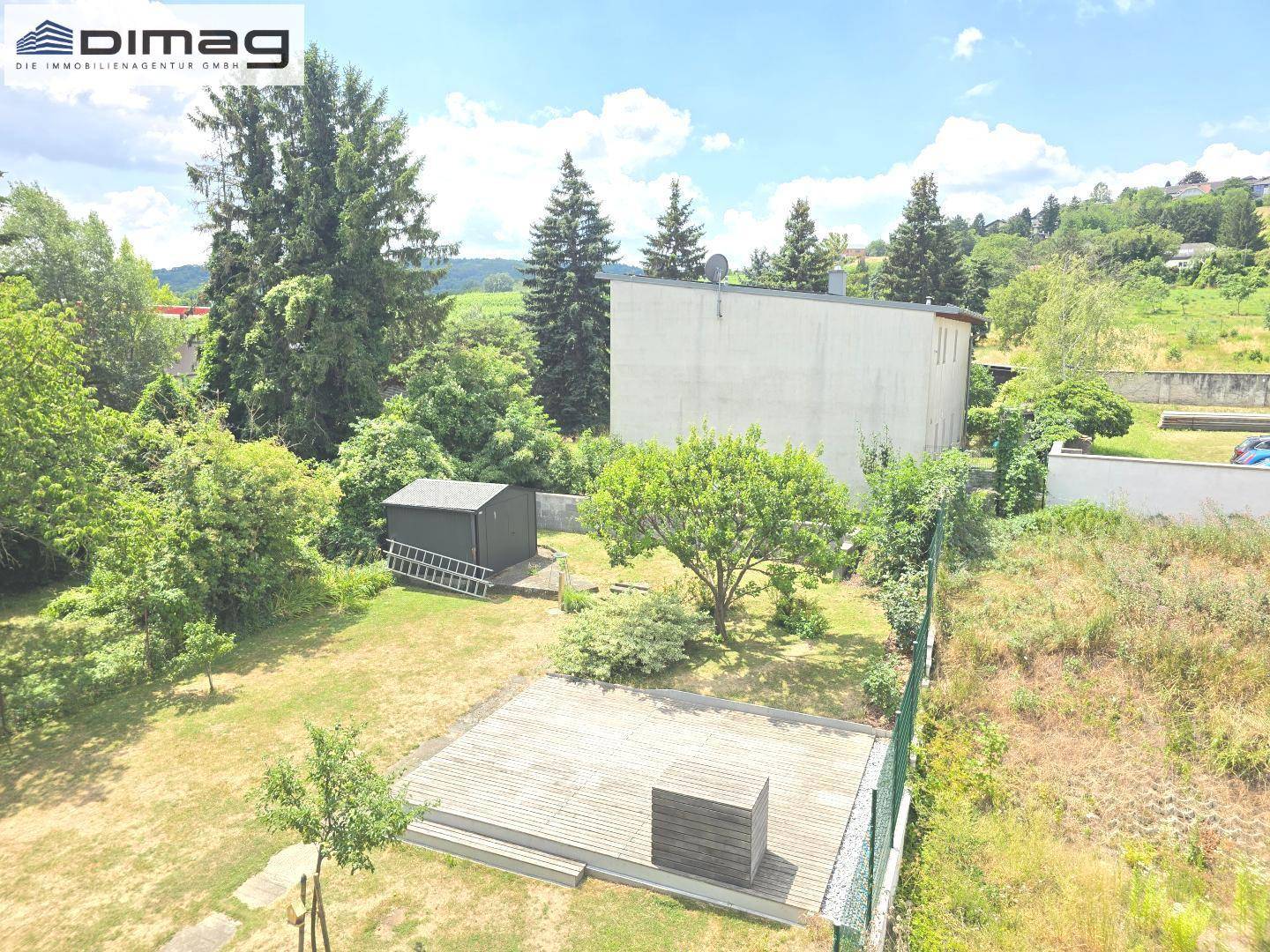 Großer Gartenbereich mit Holzterrasse, Rasenfläche und einem kleinen Geräteschuppen.