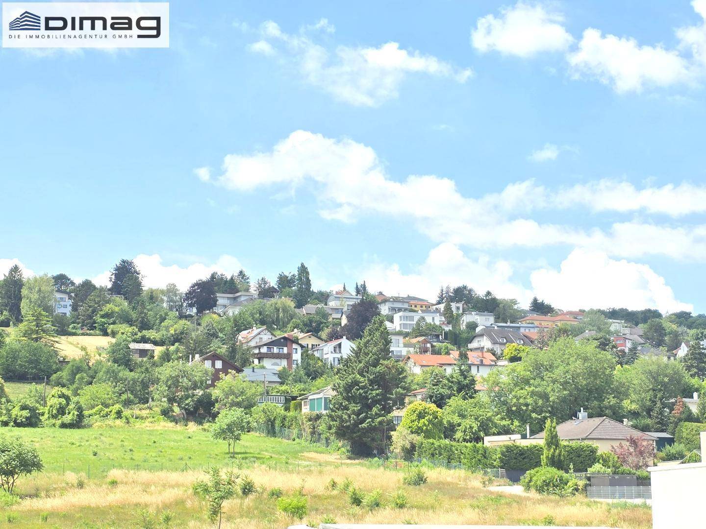 Panoramablick auf eine grüne Landschaft mit verstreuten Häusern und bewaldeten Hügeln.