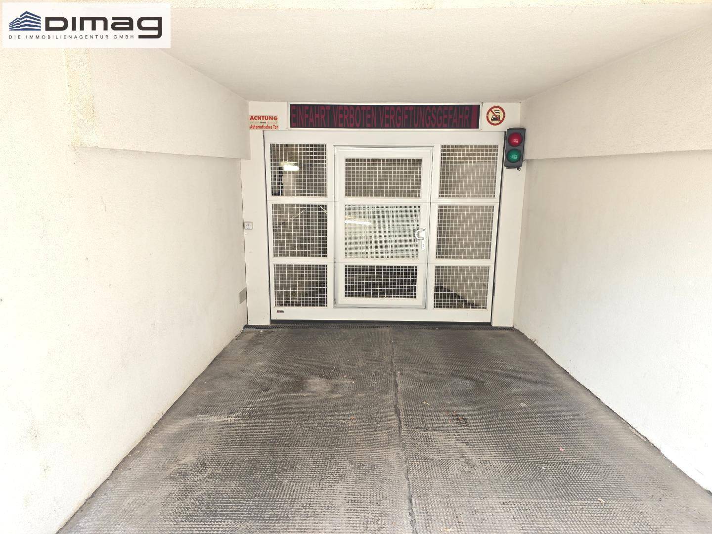 Einfahrt zur Tiefgarage mit Gittertor, Ampel und Sicherheitshinweisen.