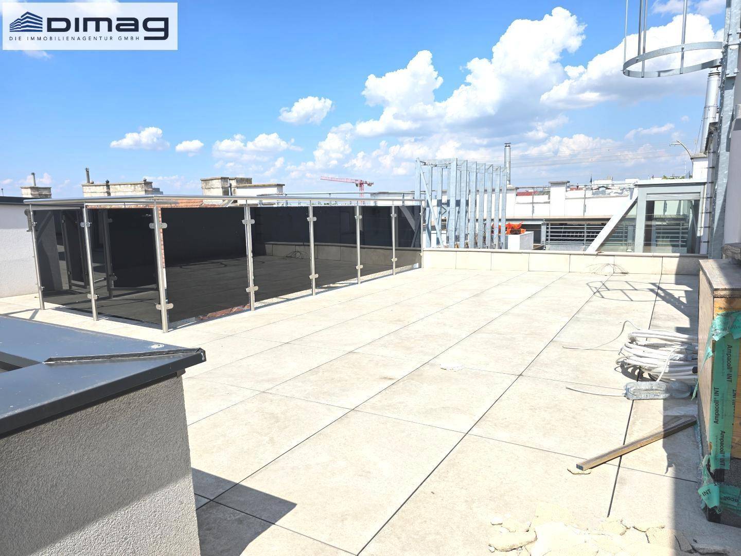 Weitläufige Dachterrasse mit Fliesenboden und Blick über die Stadt unter blauem Himmel.