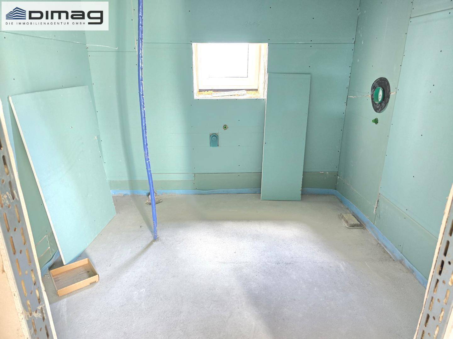 Rohbau eines Badezimmers mit Fenster und vorbereiteten Installationen für Sanitäranlagen.