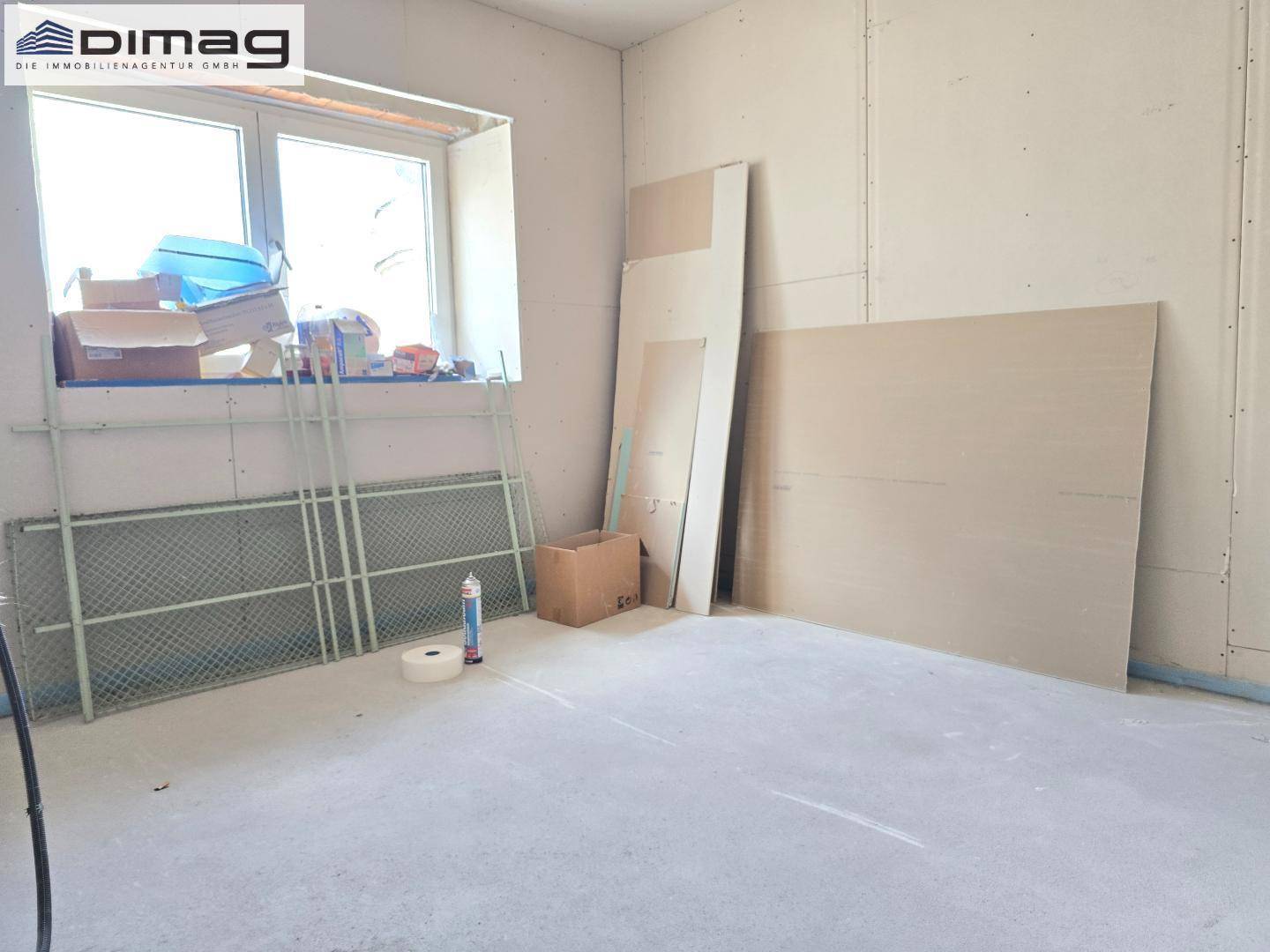 Rohbau eines Zimmers mit Fenster und Baumaterialien, bereit für den weiteren Ausbau.