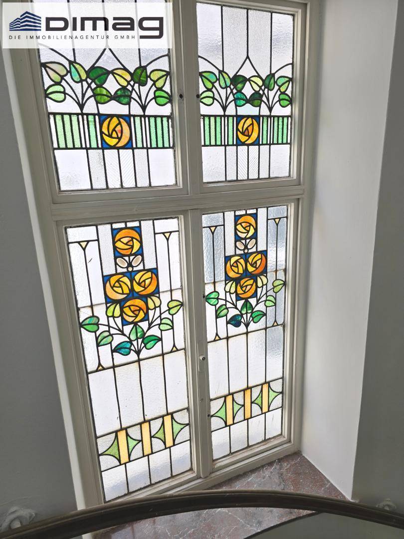 Buntes Bleiglasfenster mit floralen Mustern, das natürliches Licht in den Treppenbereich bringt.
