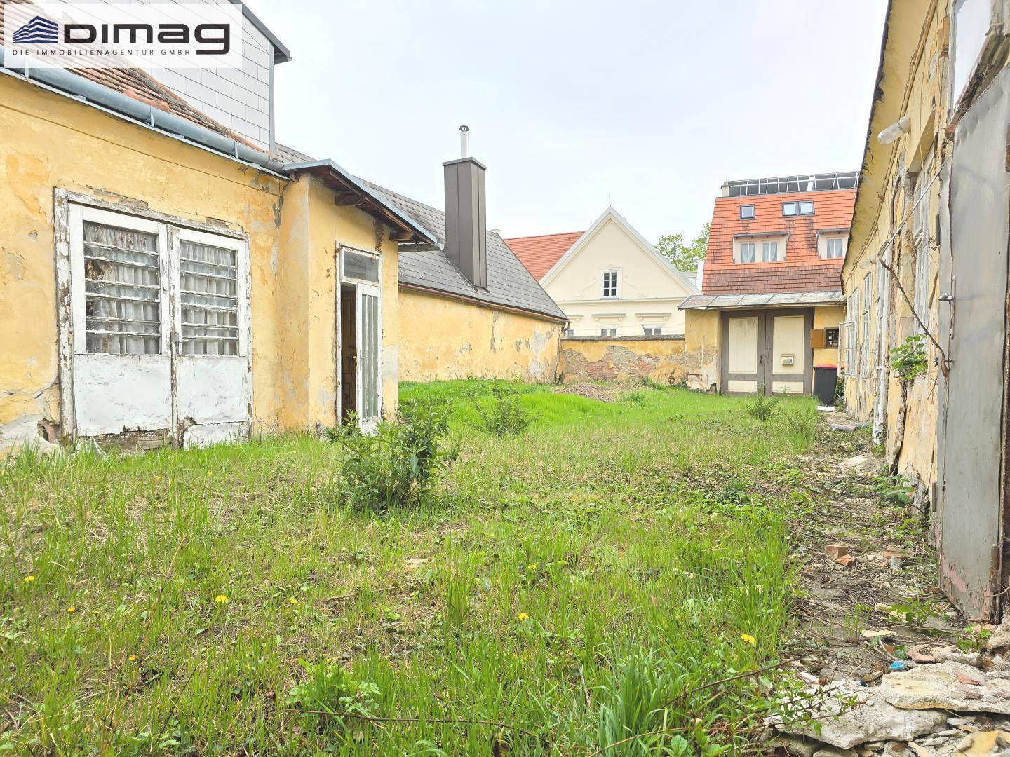 Ansicht des Innenhofs mit ungepflegtem Garten und den historischen Gebäuden, die Renovierung benötigen.