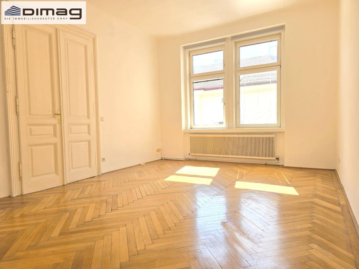 Lichtdurchflutetes Zimmer mit elegantem Fischgrätparkett und hohen Flügeltüren.