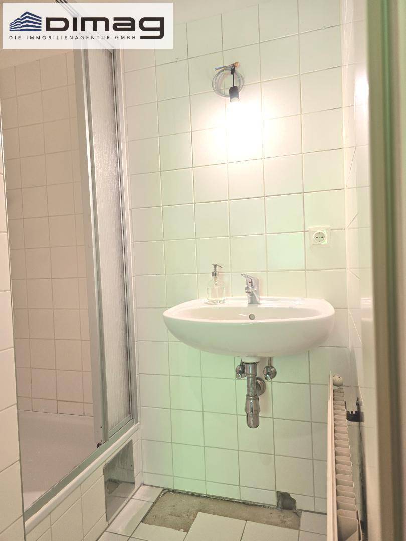 Badezimmer mit Waschbecken, Duschkabine und weißen Wandfliesen.