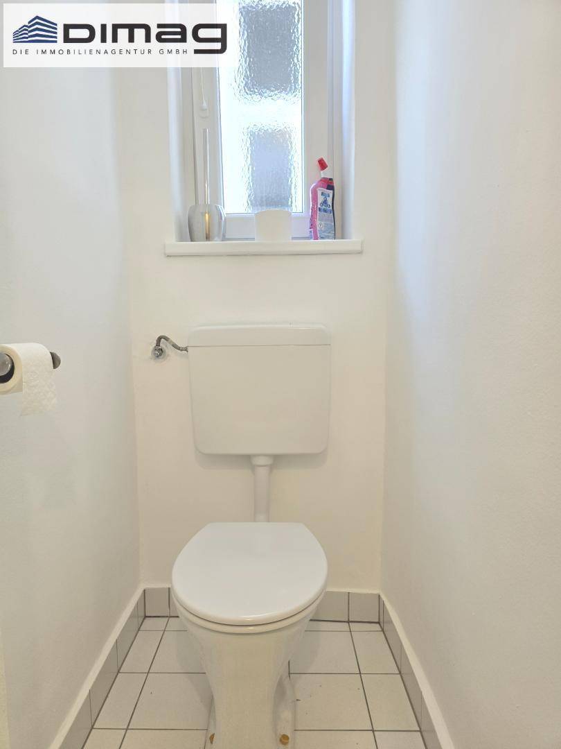Separate Toilette mit Fenster und weißen Fliesen, bietet Tageslicht.