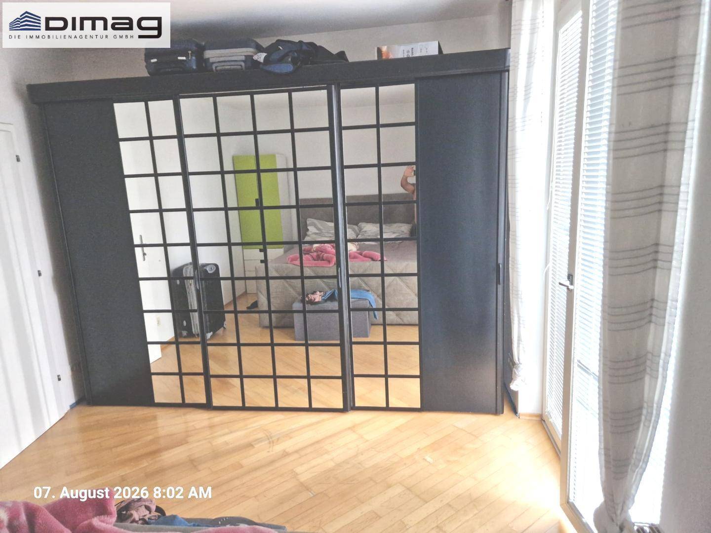 Schlafzimmer mit warmem Holzparkettboden und einem großen Spiegelschrank mit Gittermuster.