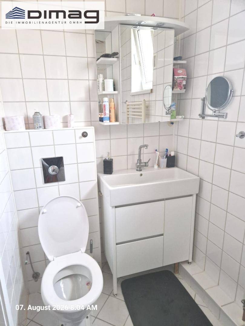 Helles Badezimmer mit WC, modernem Waschbeckenunterschrank und einem Spiegelschrank.