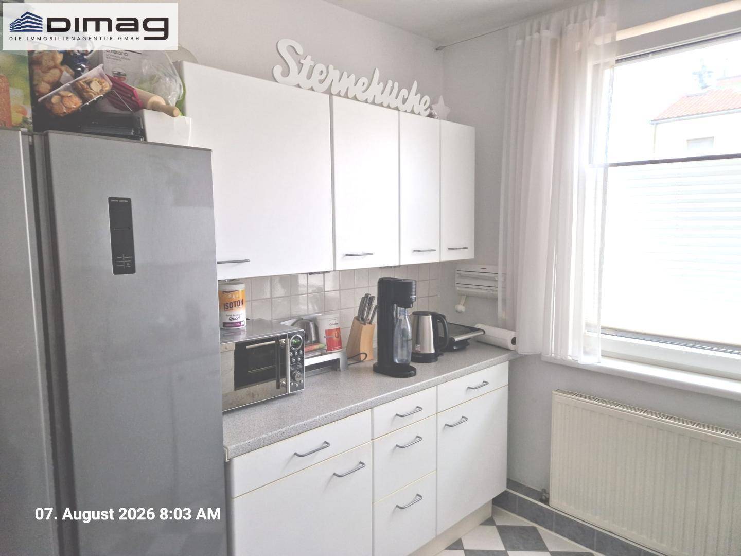 Funktionale Küche mit weißen Hängeschränken, Fliesenrückwand und einem modernen Kühlschrank.