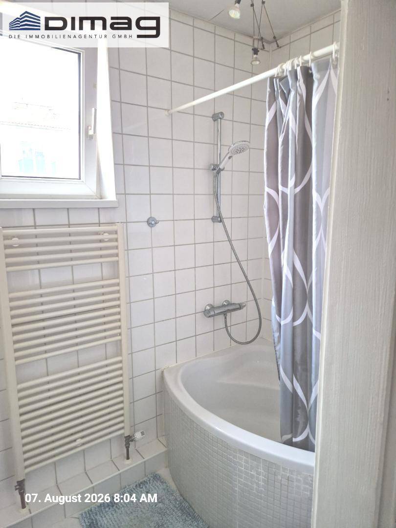 Badezimmer mit weißen Wandfliesen, einer praktischen Eckbadewanne und einem Handtuchheizkörper.