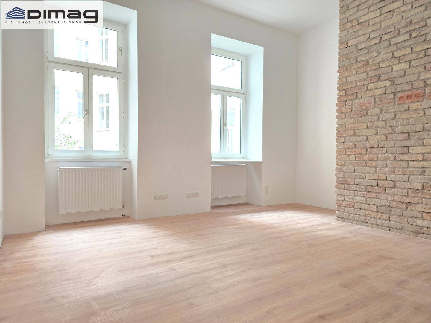 Heller Wohnraum mit Holzboden, weiß gestrichenen Wänden und einer markanten Sichtziegelwand.