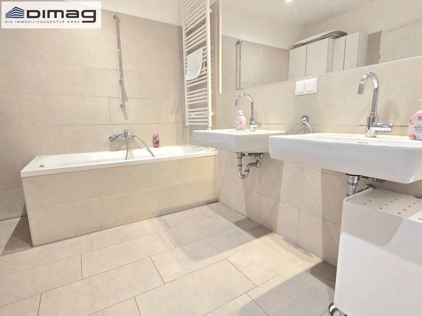 Modernes Badezimmer mit Doppelwaschbecken, Badewanne und beigefarbenen Fliesen.