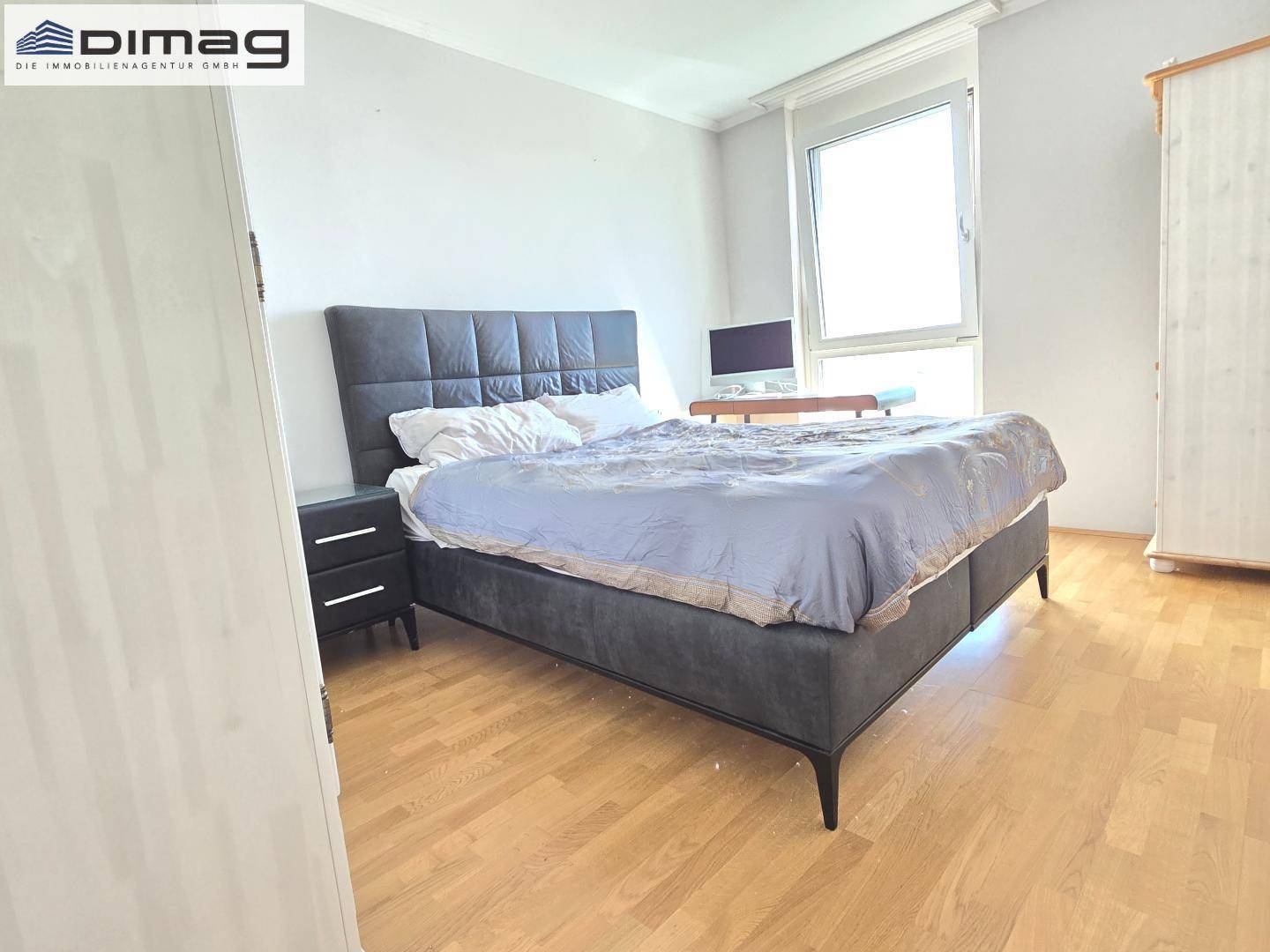 Helles Schlafzimmer mit Parkettboden, großem Bett und weißem Kleiderschrank.