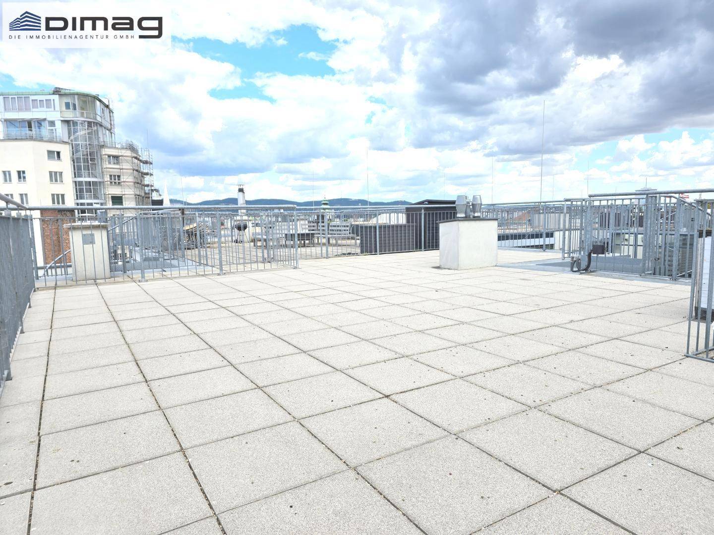 Große Dachterrasse mit Fliesenboden und weitem Blick über die umliegenden Gebäude der Stadt.