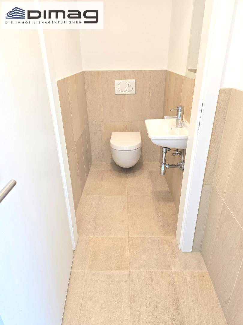 Modernes Gäste-WC mit wandhängendem WC und kleinem Waschbecken, in hellen Beigetönen gefliest.