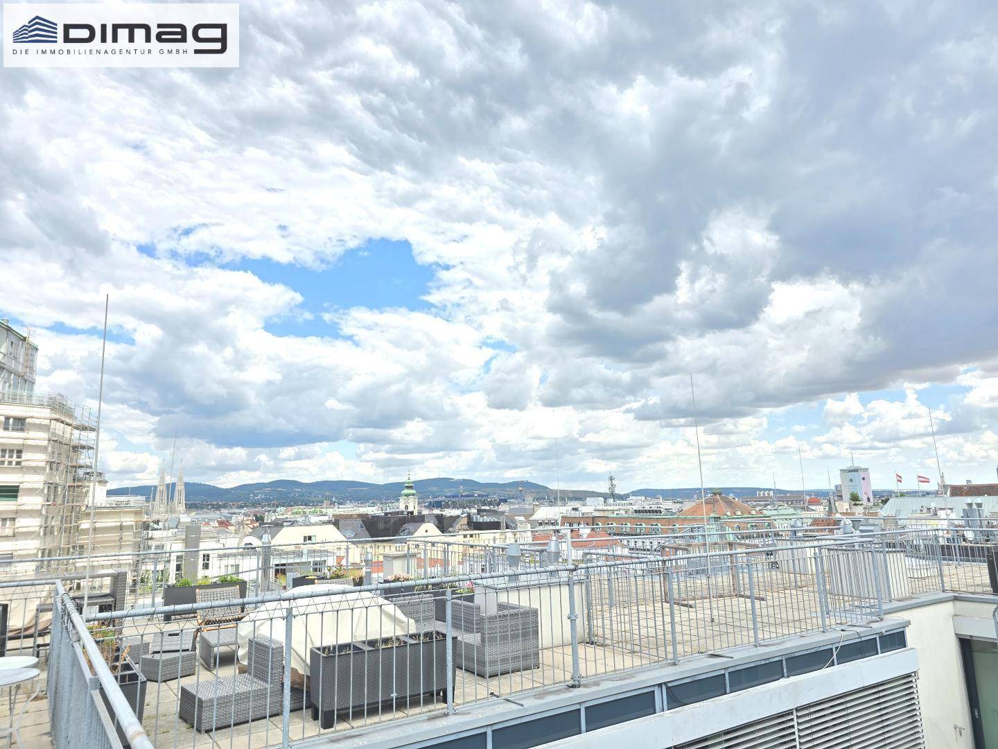 Geräumige Dachterrasse mit Sitzgelegenheiten und weitem Blick über die Stadt und die Berge im Hintergrund.