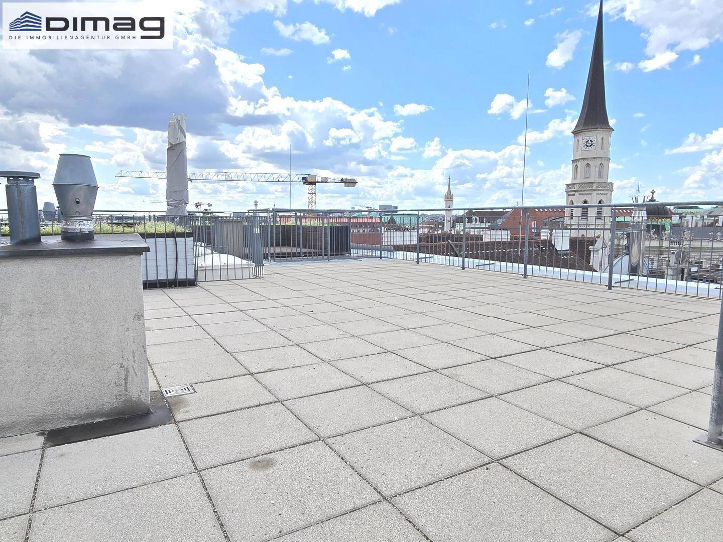 Weitläufige Dachterrasse mit Fliesenboden und Panoramablick über die Stadt und Kirchtürme.