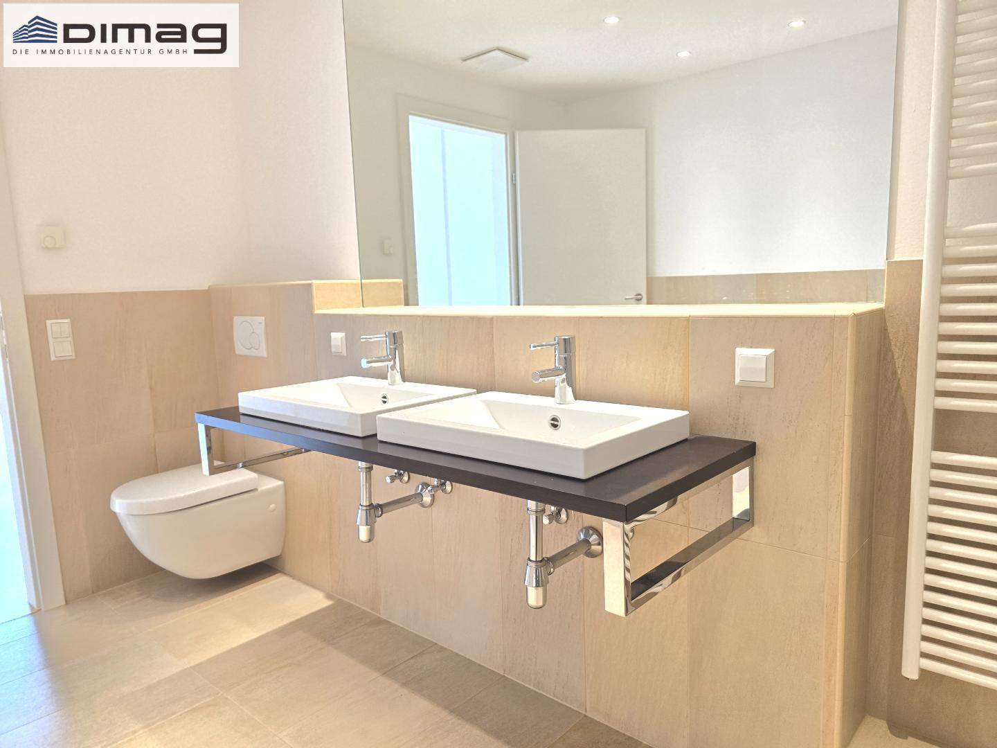 Elegantes Badezimmer mit zwei Waschbecken, wandhängendem WC und großem Spiegel.