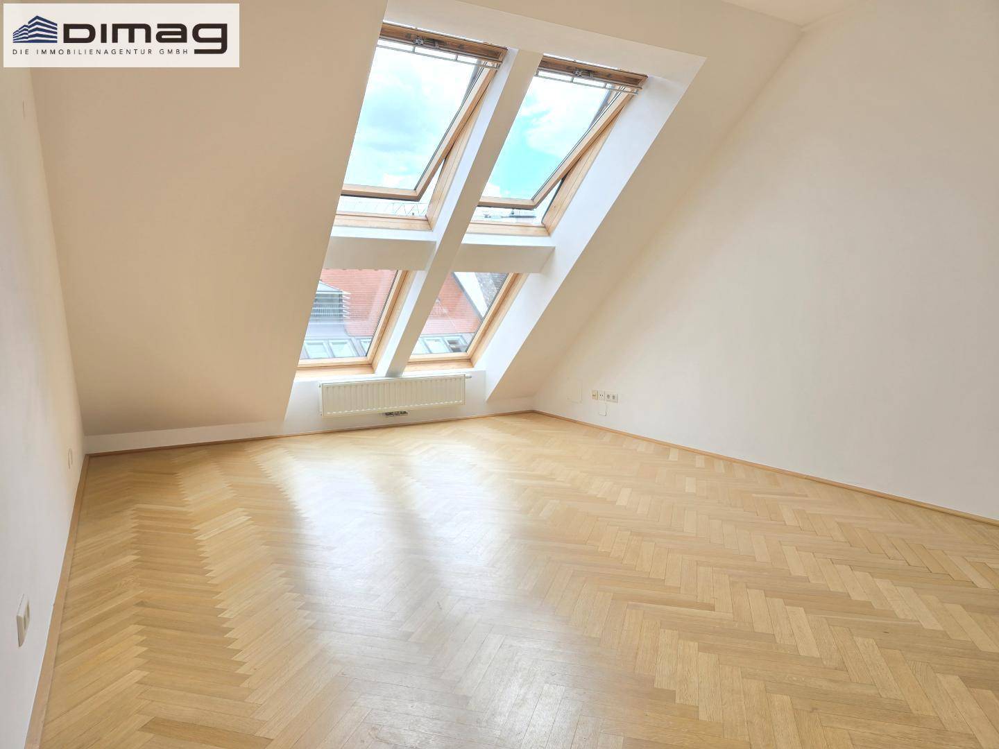 Helles Schlafzimmer im Dachgeschoss mit schrägen Wänden, Fischgrätparkett und Dachfenstern.