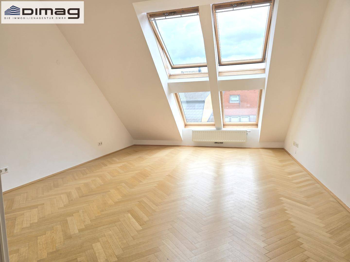 Geräumiges Dachgeschosszimmer mit Fischgrätparkett und mehreren Dachfenstern für viel Tageslicht.